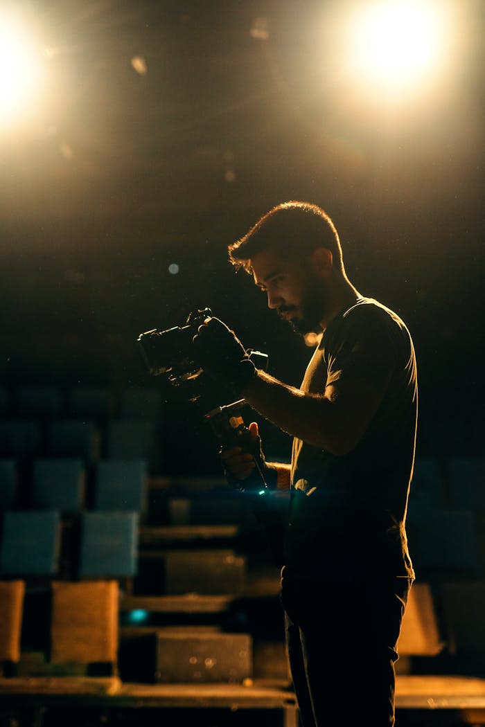 A filmmaker adjusts his camera under bright stage spotlights, creating a dramatic scene.