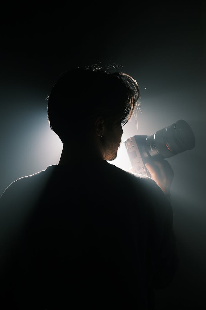 Artistic silhouette of a photographer holding a camera with striking backlight, creating a moody atmosphere.